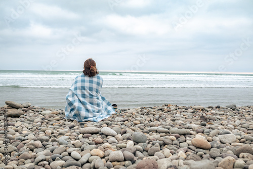 Tableau sur toile A woman sitting on a beach with a blanket. Copy space
