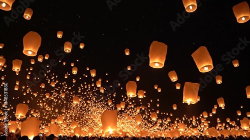 Thousands of glowing sky lanterns ascend into the dark night sky during a festival