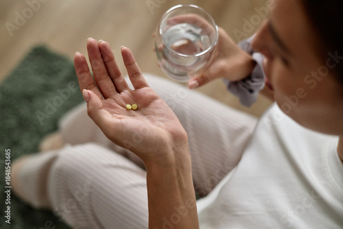 Photos Young adult Caucasian woman sitting and holding two pills in one hand while hold