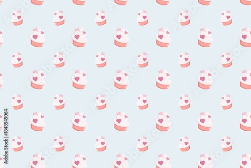 Seamless pattern of cute pink cupcakes with heart toppings on a soft pastel blue background. Sweet romantic design for wrapping paper, textiles, stationery, party decor and Valentine theme