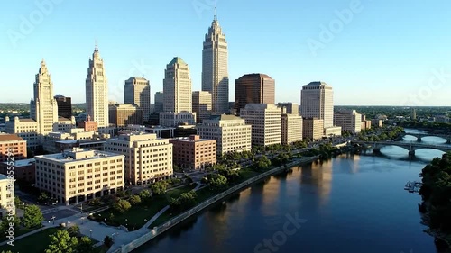 A sunlit downtown skyline with classic architecture towers along a calm river