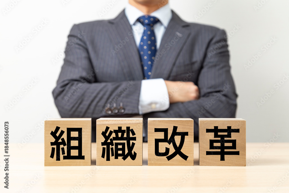 Obraz premium 「組織改革」と書かれたブロックと腕組みをするビジネスマン