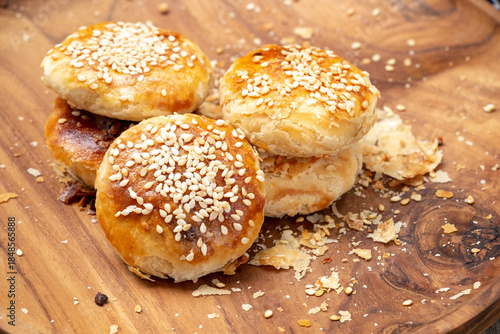 Traditional Indonesian bakpia pastry with mung bean filling on a wooden plate. Close-up high-angle shot of a flaky snack with crumbs and a checkered cloth detail.