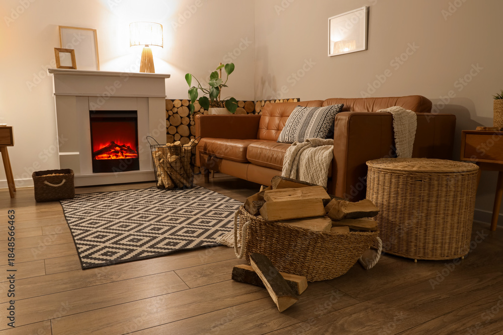 Fototapeta premium Interior of living room with sofa, fireplace and firewood in wicker basket at night