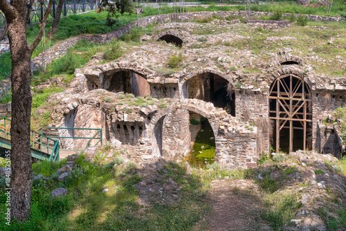 Byzantine Cistern, Kadifekale castle, Izmir, Turkey. Ancient stone arches and structures, partially overgrown with green grass and trees. Historic ruins.