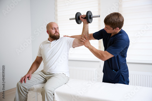 Quadro em tela Physiotherapist assisting male patient with shoulder rehabilitation exercise using dumbbell