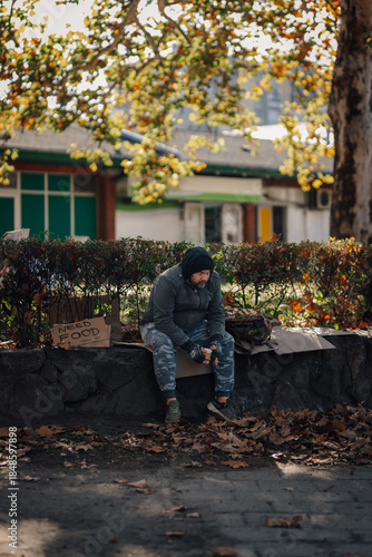 Homeless man sitting on street with 'need food' sign