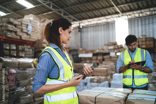 Two people in yellow vests are looking at their phones in a warehouse