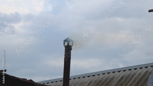 Smoke from a small chimney against a cloudy sky. A small rural bathhouse is being heated