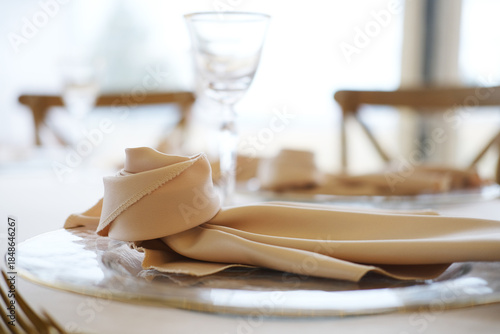 Fotografia Table setting with beige napkin elegantly arranged on silver plate beside glassw
