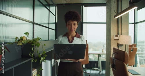 Individual analyzes computer amid open office and city backdrop