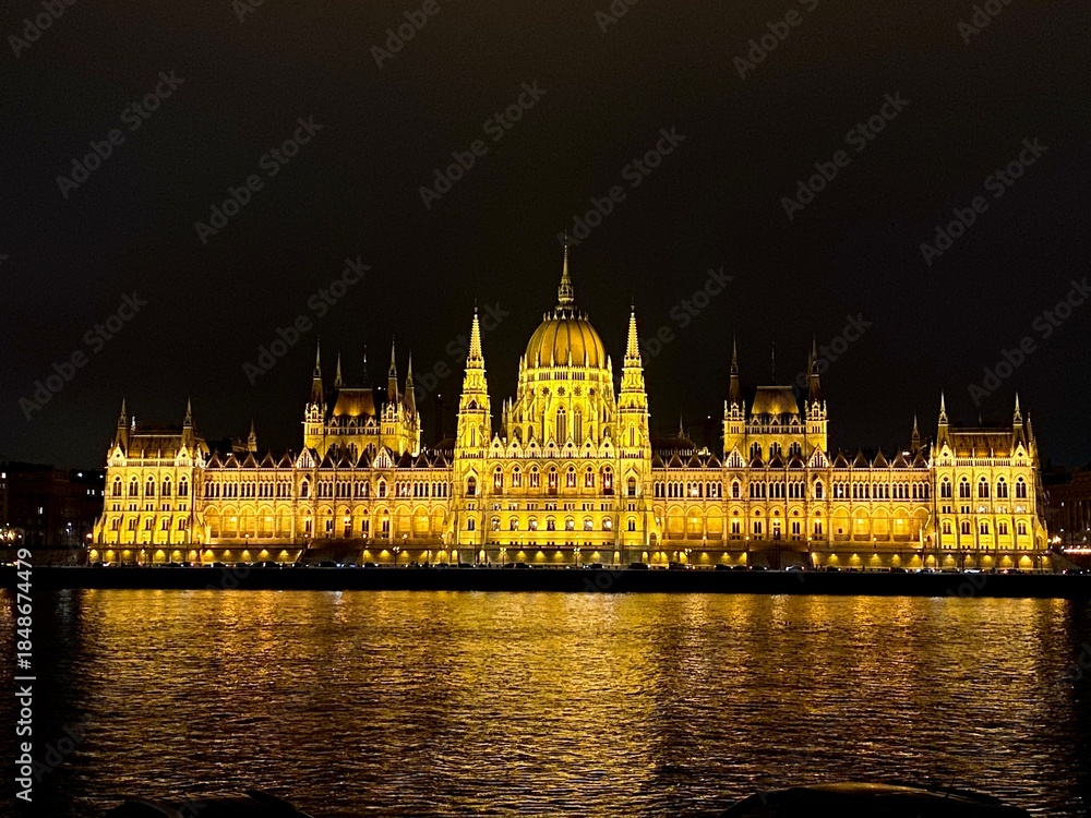 Fototapeta premium Parliament glowing brightly at night in Budapest, Hungary. View across the Danube River.