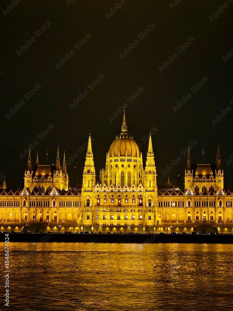 Fototapeta premium Parliament glowing brightly at night in Budapest, Hungary. View across the Danube River.