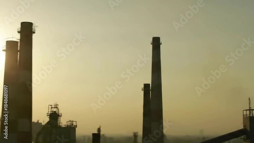 Industrial smokestacks silhouetted against the sunset, showcasing manufacturing activity and urban landscape dynamics. Ideal for articles on environmental issues or industrial growth.