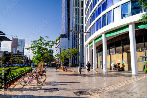 Parked bicycles on Tel Aviv street with people walking and glass office buildings in the financial district, Israel.