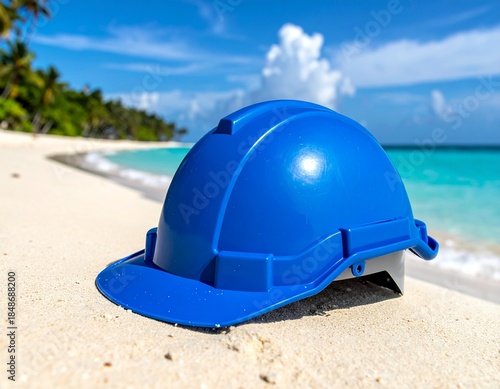 Blue hard hat on a sandy beach with ocean and sky background, concept of work and vacation.
