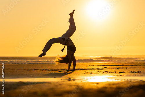Obraz na plátne Woman performing capoeira cartwheel on beach at sunset