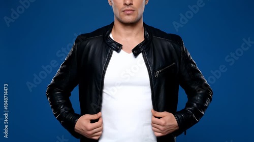 Man Wearing A Black Leather Jacket Open Revealing A White T Shirt Against A Solid Blue Background Studio Portrait