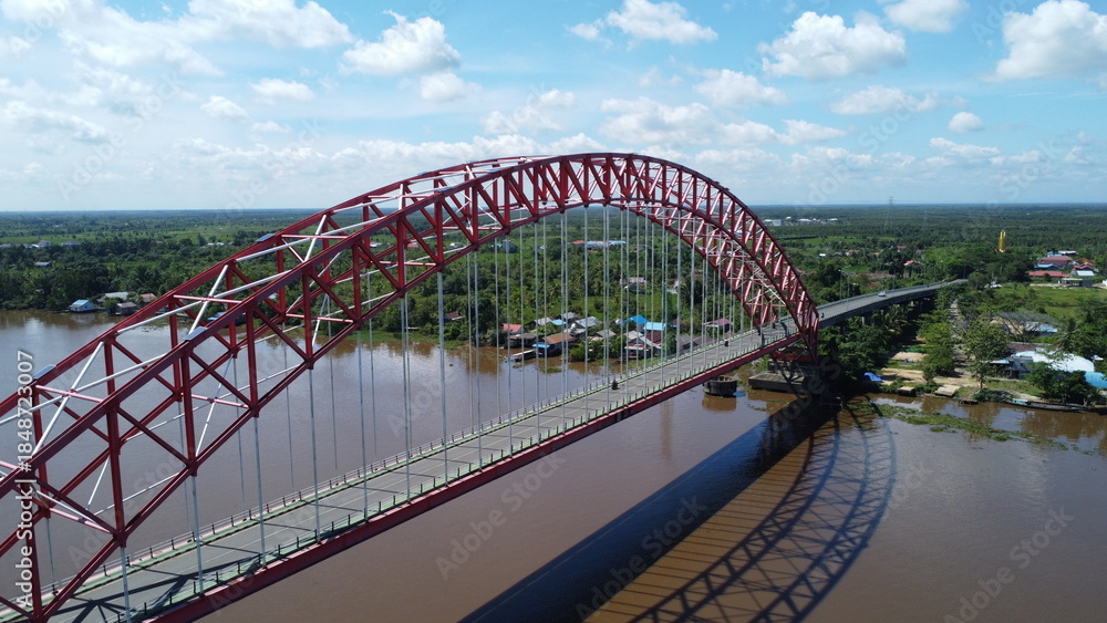 Obraz premium Aerial view of a tugboat pulling a barge filled with coal across the Rumpiang Bridge in the waters of South Kalimantan, Barito River