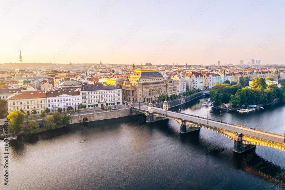 Fototapeta premium The National Theatre stands prominently along the Vltava River in Prague, capturing the golden tones of sunset.