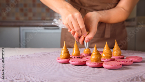 woman pastry chef extrudes cream onto macaroon halves using pastry bag. cream mass pyramid