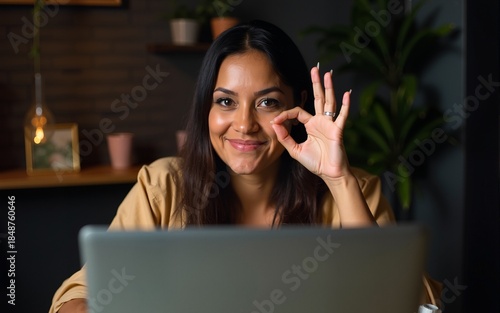 Middle age hispanic woman working using computer laptop late at night smiling happy doing ok sign with hand on eye looking through fingers. High quality