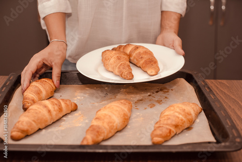 woman moving freshly baked croissants from hot baking sheet to plate