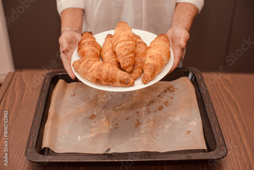 woman hands holding freshly baked croissants on white plate under hot baking sheet