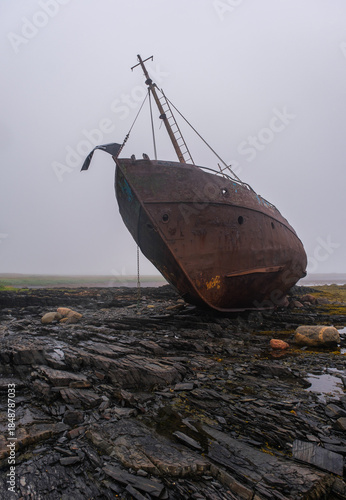 An old fishing schooner is stuck on the rocky Barents Sea, Rybachy Peninsula. The vessel is covered in rust