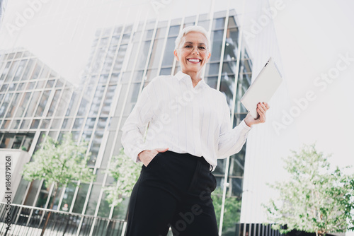 Obraz na płótnie Confident elderly businesswoman stands outdoors in a modern cityscape smiling wh