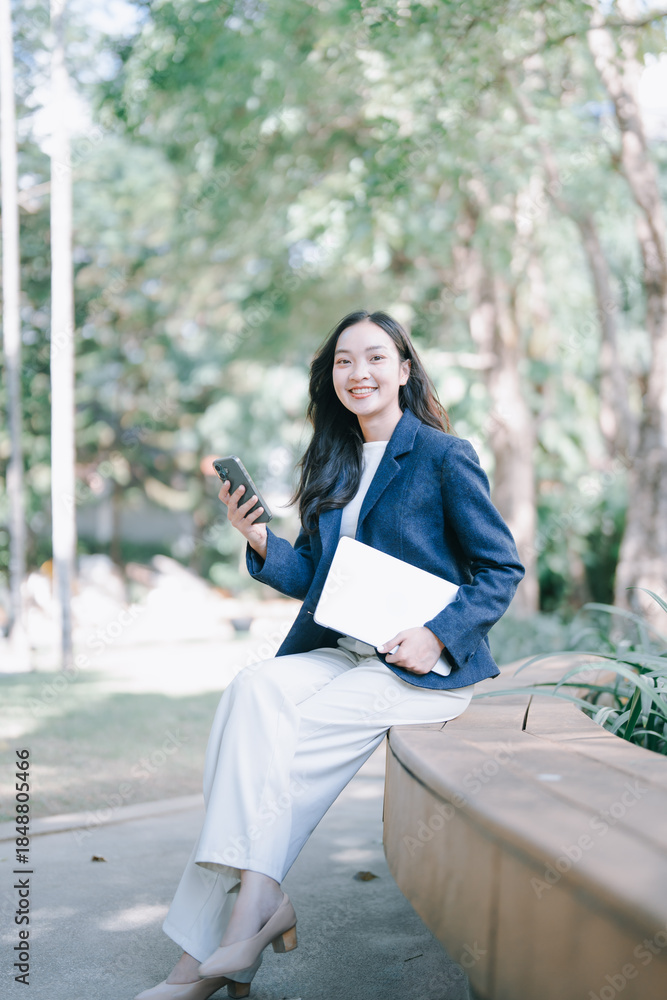 Naklejka premium Young Asian professional woman smiling with smartphone and laptop