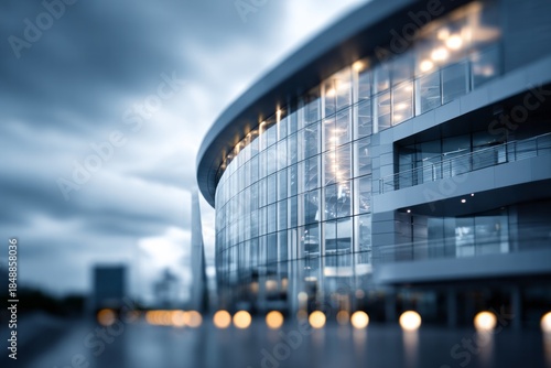 Modern curved glass structure illuminated against a dramatic overcast sky