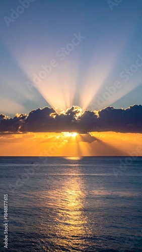 Radiant sunlight beams from behind clouds over a calm ocean, with sparkling reflections on water