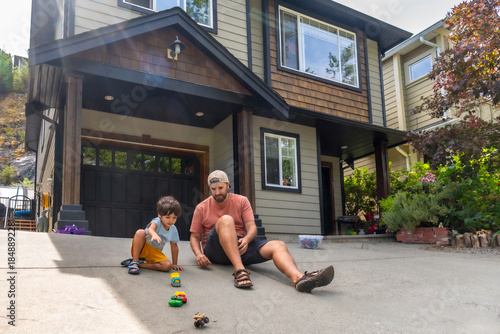 Bild auf Leinwand Father and son playing with toy cars on driveway of suburban home