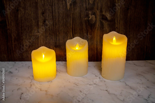 Festive three yellow candles on a dark brown board background. Holiday, Christmas, New Year, postcards.