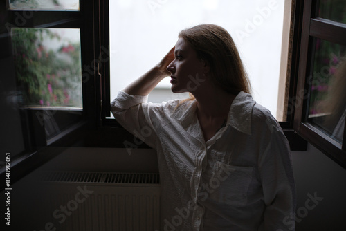 Woman in thoughtful silhouette by window in low light
