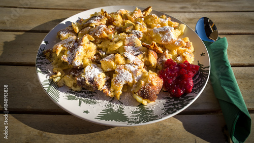 eating outside on a ski lodge - Austrian specialty a kaiserschmarrn with raisins, apple and cranberry jam served on a decorative plate on a wood table at a sunny winter day