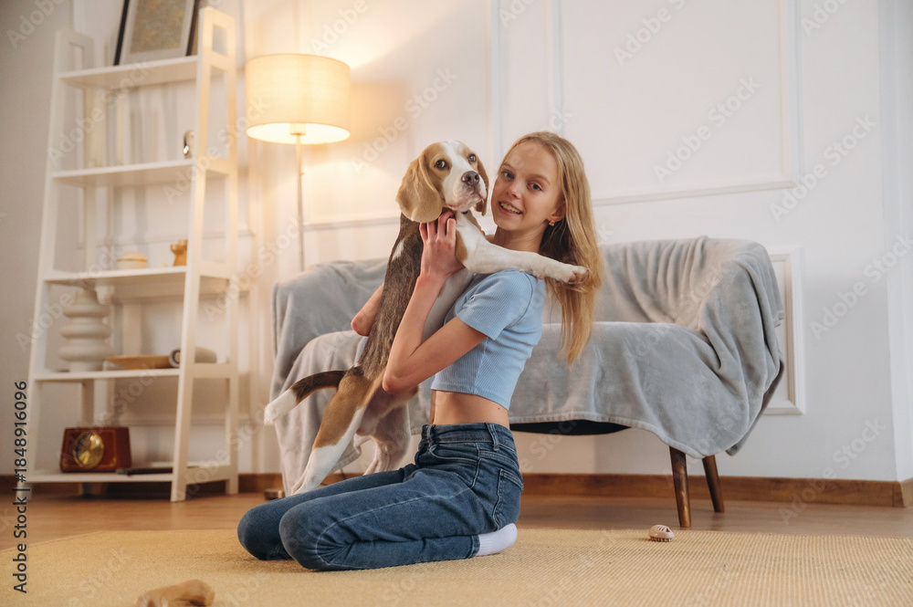 Naklejka premium Side view, sitting. Girl is with her dog on the floor in a cozy living room