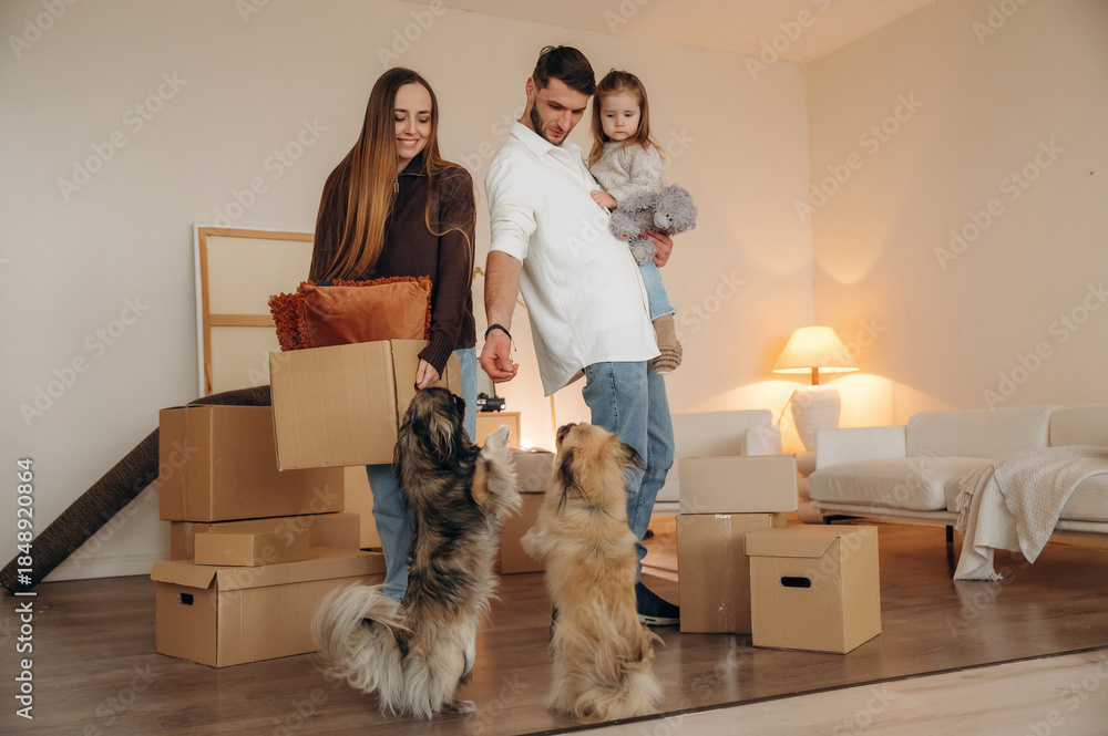 Fototapeta premium Conception of new life. Happy young family with child and dog moving into new home, standing among cardboard boxes
