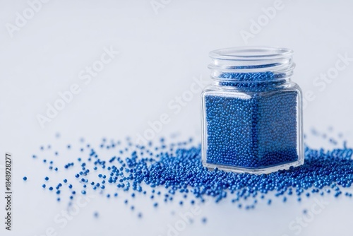 Small glass jar filled with blue beads spilling out on white surface background