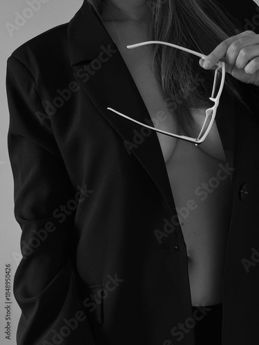 A girl in a jacket on a naked body with glasses in her hands, her face is not visible. Boudoir photo shoot of a girl