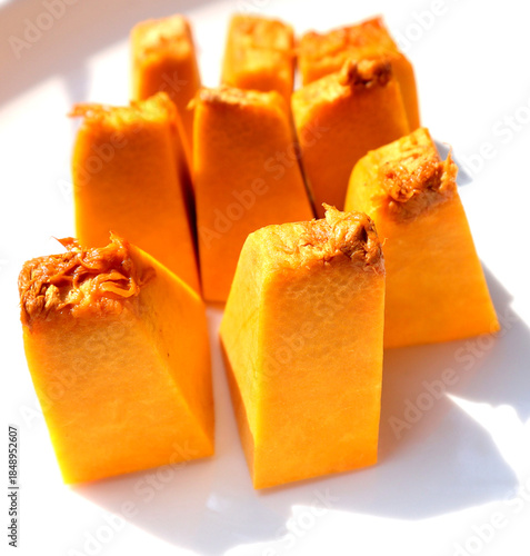 Several cubes of bright orange steamed pumpkin arranged on a white surface.