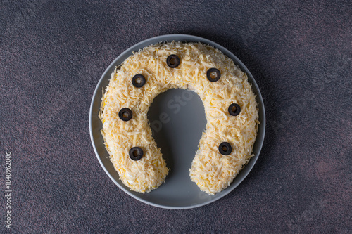 Festive salad in shape of horseshoe with chicken, eggs, cheese and olives on brown table, Top view