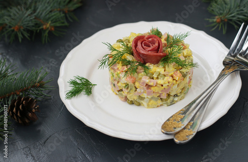 Homemade salad Olivier with sausage, peas and potatoes on white plate on gray background