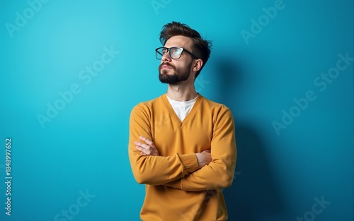 Young handsome man with beard wearing casual sweater and glasses over blue background looking to the side with arms crossed convinced and confident. High quality