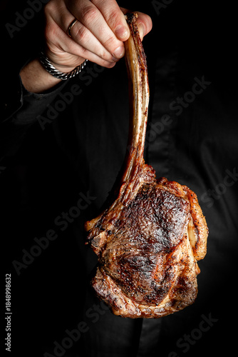 Foto A tomahawk steak held by a person in dark attire, professionally grilled with a long bone, against a black background