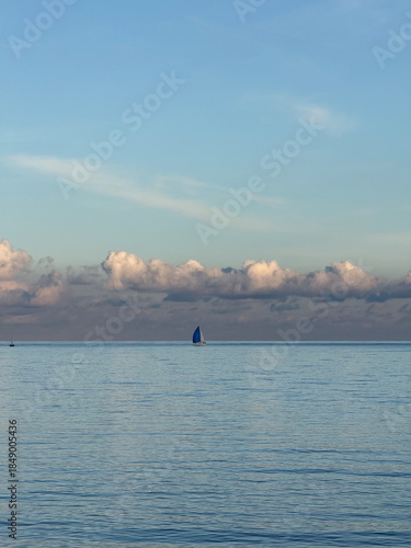 Sailboats floating on a quiet ocean during gentle light, with dramatic clouds lining the horizon. Serene marine landscape ideal for travel, freedom, and relaxation concepts.