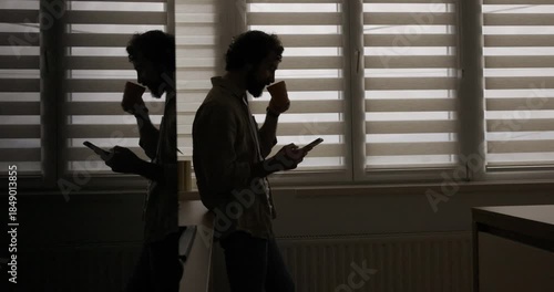 Man Enjoying Morning Coffee While Using Smartphone in Silhouette by Window