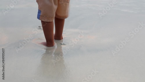 barefoot child standing in calm sea water at shoreline