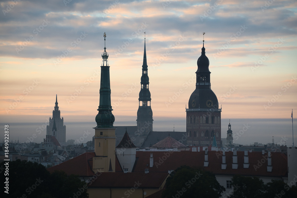 Naklejka premium Blick über die Dächer von Riga in Lettland in der dunstigen Morgendämmerung mit den Turmspitzen mehrerer Kirchen in den Silhouetten